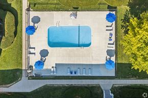 Rochester apartment for rent - An aerial view of a pool surrounded by a concrete deck and blue umbrellas.