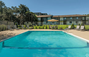 Madison apartment for rent - A large swimming pool in front of a building with a lawn and trees in the background.