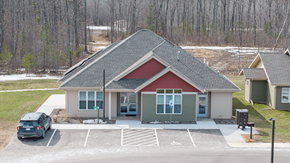 Lac Du Flambeau apartment for rent - A small building with a red roof is surrounded by a parking lot.