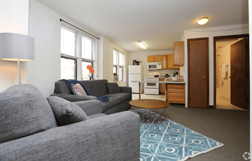 Madison apartment for rent - A grey couch with a blue throw pillow sits in a living room with a kitchen in the background.