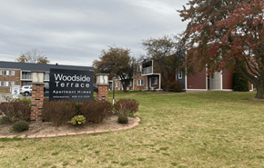 Beloit apartment for rent - A sign for Woodside Terrace Apartment Homes is displayed in front of a grassy area.