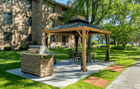 Madison apartment for rent - A wooden gazebo with a grill is situated in a grassy area in front of a building.