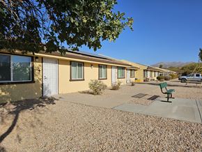 Kearny apartment for rent - A sunny day at the mobile home park with a bench and a tree in the foreground.