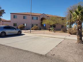 Eloy apartment for rent - A silver car is parked in front of a pink building with a blue handicap sign.
