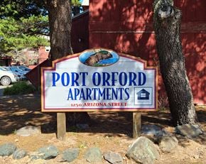Port Orford apartment for rent - A sign for Port Orford Apartments is displayed in front of a tree.