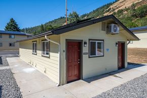 White Salmon apartment for rent - A small house with a brown door and a red door is surrounded by a gravel driveway.