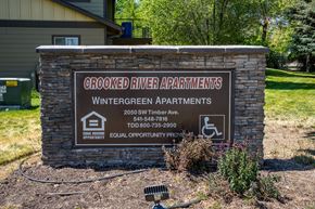 Redmond apartment for rent - A sign for Crooked River Apartments is displayed in front of a building.