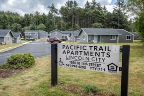 Lincoln City apartment for rent - A sign for Pacific Trail Apartments in Lincoln City is displayed in front of a row of houses.