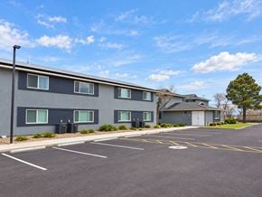 Chino Valley apartment for rent - A parking lot in front of a grey building with a blue sky and clouds in the background.