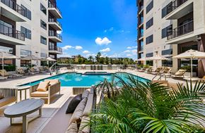 Phoenix apartment for rent - A pool surrounded by chairs and plants with apartment buildings in the background.