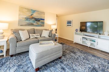 Baltimore apartment for rent - A living room with a grey couch, a grey ottoman, a television, and a painting on the wall.
