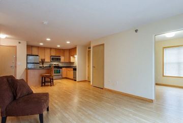 Grand Forks apartment for rent - A brown couch is in a living room with a kitchen in the background.