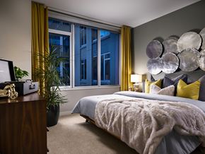 Denver apartment for rent - A model bedroom with a large window, a queen sized bed, and a vanity at The Quincy in Downtown Denver.