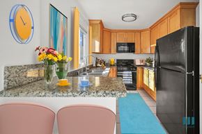 Los Angeles apartment for rent - A kitchen with a black fridge, pink chairs and a clock on the wall.