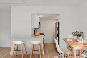 New Smyrna Beach apartment for rent - A kitchen with white walls and wooden floors, featuring a bar area with stools, a dining table with chairs, and a refrigerator.
