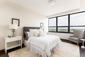 South Bend apartment for rent - A bedroom with a large bed, a nightstand with a lamp, a chair, and a window with a view.