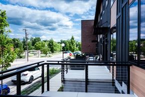 Plymouth apartment for rent - A balcony with a railing overlooks a parking lot and trees.