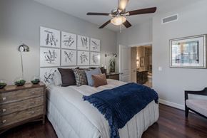 Houston apartment for rent - A bedroom with a bed, a ceiling fan, and a wall with pictures.