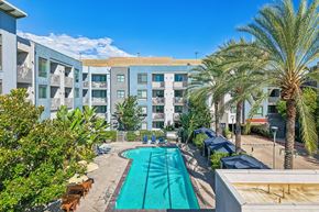Northridge apartment for rent - A swimming pool in front of a building surrounded by palm trees.