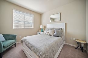 Northridge apartment for rent - A bedroom with a bed, a green chair, a nightstand with a lamp, and a mirror on the wall.
