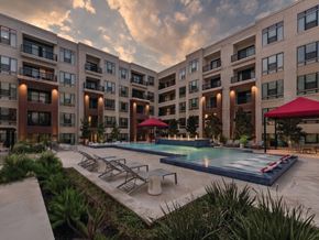 Houston apartment for rent - A large swimming pool is surrounded by lounge chairs and umbrellas in front of apartment buildings.