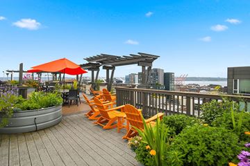 Seattle apartment for rent - A wooden deck with orange chairs and a red umbrella overlooking a city skyline.
