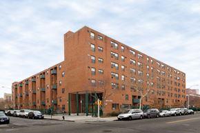 Bronx apartment for rent - A large red brick building with a green fence in front.