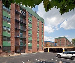 Brooklyn apartment for rent - A red brick building with a green roof and a parking lot in front.