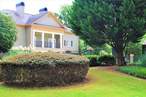 Clarkston apartment for rent - A house with a grey roof and a yellow trim is surrounded by a green lawn and a hedge at Woodside Village Apartments, Clarkston, GA 30021