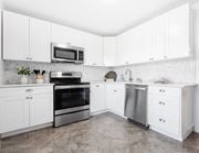 Roseland triplex for rent - A bright and spacious kitchen with white cabinets, herringbone tile backsplash, stainless steel appliances, and tile-style flooring.