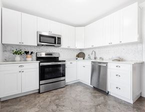 Roseland triplex for rent - Modern white kitchen with white cabinets, herringbone tile backsplash, stainless steel appliances, and tile-style flooring at Everly Roseland apartments in Livingston, NJ.