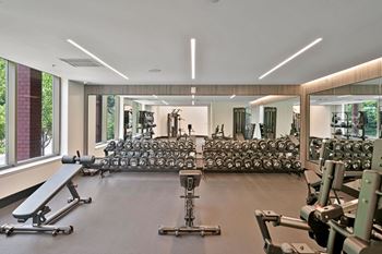 A gym with weights and cardio equipment in a building with large windows