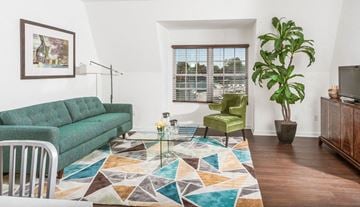 Milford apartment for rent - A living room with a green couch, a green chair, a glass coffee table and a potted plant.