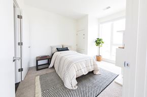 Detroit apartment for rent - A bedroom with a bed, pillows, a small table, and a potted plant.
