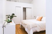 Detroit apartment for rent - a bedroom with white walls and a white bed with an orange pillow at The Ferguson Apartments, Detroit, 48226