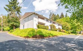 Vancouver apartment for rent - A white building with a brown roof is surrounded by greenery.