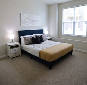 Saukville apartment for rent - A bedroom with a bed, nightstand, and a painting on the wall at The Daniels at Northern Gateway Apartments, Saukville, WI, 53080
