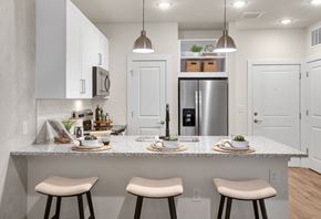 Lawrenceville apartment for rent - Dog-Friendly Luxury Apartments in Pleasant Hill, GA - Celadon on Club - Kitchen with a Breakfast Bar, Stools, Granite Countertops, Tile Backsplash, Pendant Lighting, and Stainless Steel Appliances.