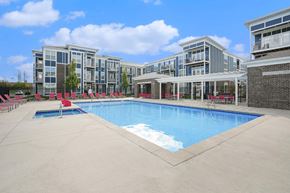 Grand Rapids apartment for rent - Three-Bedroom Apartments in Grand Rapids, MI - Knapp’s Corner Flats - Resort Style Pool With Spacious Sundeck, Red Lounge Chairs, Covered Seating, And Modern Apartment Buildings.