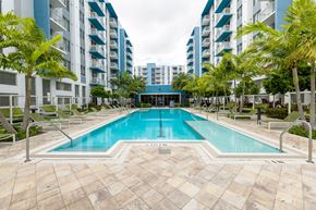 Hialeah apartment for rent - A swimming pool surrounded by palm trees and lounge chairs in front of apartment buildings.