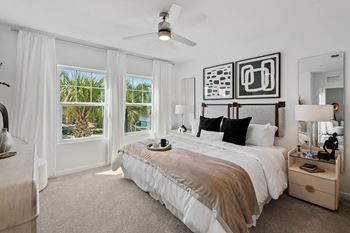 A bedroom with a large bed, a ceiling fan, and a view of the outdoors through the windows
