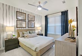 Lawrenceville apartment for rent - Pet-Friendly Luxury Apartments in Pleasant Hill, GA - Celadon on Club - Bedroom with Carpet Flooring, Large Bed, Nightstands, Lamps, Dresser, Ceiling Fan with Lighting, Wall Arts, and Large Window.