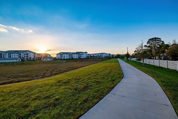 A pathway leads through a grassy area with a sunset in the background.