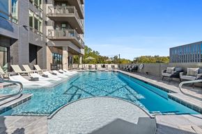 Huntsville apartment for rent - Huntsville, AL, Luxury Apartments Near Redstone Arsenal - Arcadia - Heated Saltwater Pool Featuring a Tanning Ledge, Lounge Chairs, Armchairs with Pillows, and a Background of Lush Greenery.