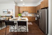 Decatur apartment for rent - Decatur, GA, Apartments Near Marta Station - Arlo - Living Room With Black Sofa, Round Wood Coffee Table, Wall-Mounted Television, Dining Area, And Modern Kitchen In The Background.