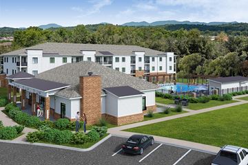 Knoxville apartment for rent - A large white building with a grey roof and a brick chimney is surrounded by a parking lot.