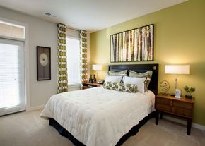 Charlotte apartment for rent - Three-Bedroom Apartments in Charlotte, NC - Gramercy Square at Ayrsley - Bedroom with Carpet Flooring, Bed, Nightstands, Lamps, Large Wall Art, Clock, Glass Door, and Large Window.