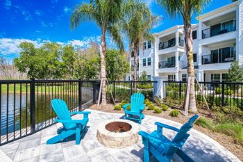 A patio with blue chairs and a fire pit in front of an apartment building
