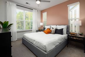 Belmont apartment for rent - One-Bedroom Apartments in Belmont, NC - Banks at Mt. Holly - Bedroom with Carpeted Floor, Large Bed, Nighstands with Lamps, Dresser, Large Windows with Blinds and Curtains, and Ceiling Fan