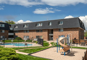 Colorado Springs apartment for rent - A playground with a slide and swimming pool in front of a brick building.